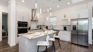 A modern kitchen with white cabinetry, stainless steel appliances, and a central island with bar stools. - Your Ultimate Luxury Getaway in the Providence Golf Community (Davenport)