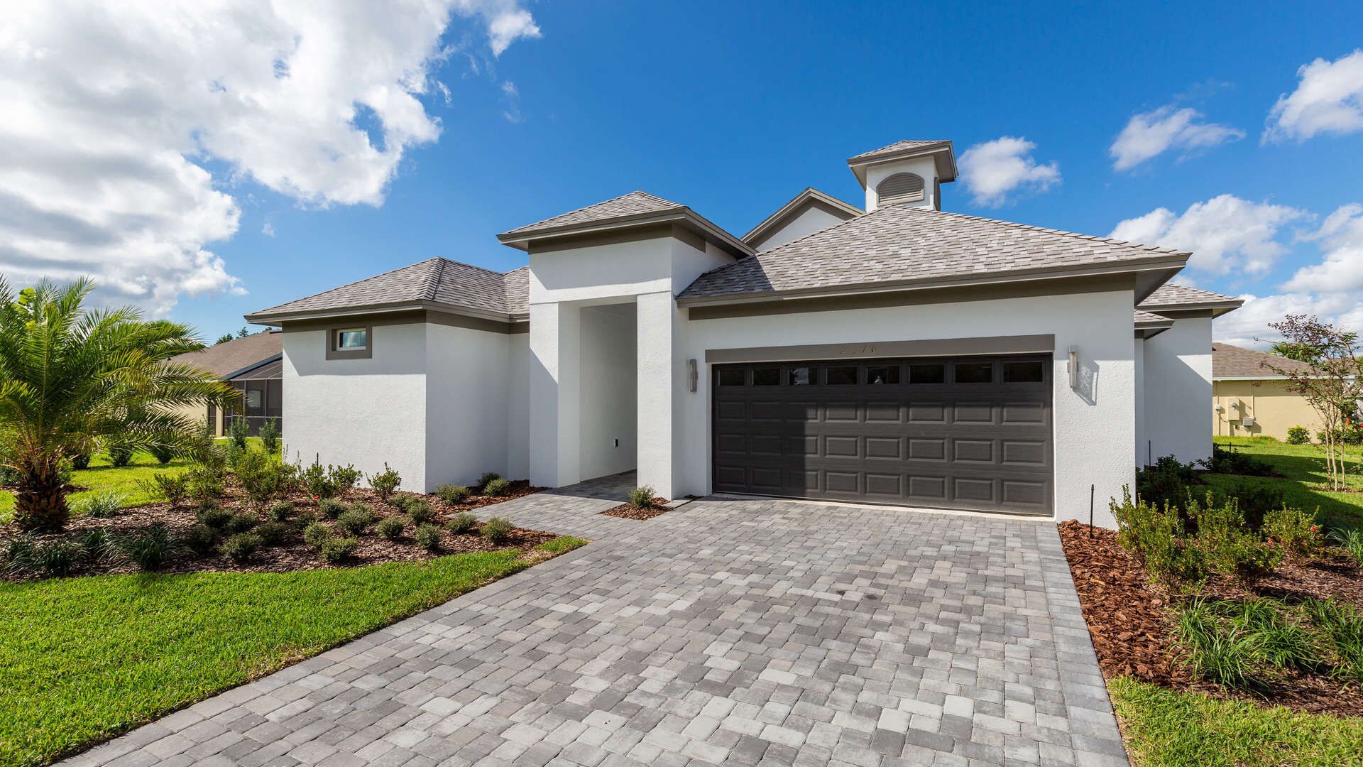 A modern two-story house with a grey driveway, a garage, and a well-maintained lawn with various plants.