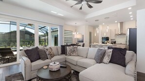 A modern living room with a sectional sofa, a dining area, and a kitchen. - Your Ultimate Luxury Getaway in the Providence Golf Community (Davenport)
