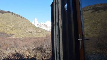 A rustic wooden building with a metal door, overlooking a mountainous landscape with sparse vegetation and a clear sky.