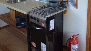 Une cuisine de taille réduite équipée d’une cuisinière à gaz, d’un évier et d’un extincteur.