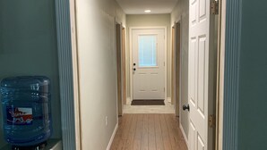 A hallway with wooden flooring, white doors, and a water dispenser on the left. - PERFECTLY CUTE COUNTRY BARDOMINIUM ON 11 ACRES (Bedias)