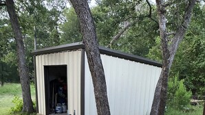 A small shed with a concrete pathway leading to it, surrounded by trees and grass. - PERFECTLY CUTE COUNTRY BARDOMINIUM ON 11 ACRES (Bedias)