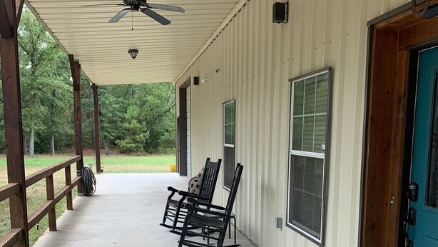 A covered porch with a ceiling fan, two rocking chairs, and a blue door. - PERFECTLY CUTE COUNTRY BARDOMINIUM ON 11 ACRES (Bedias)