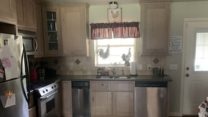 A kitchen with wooden cabinets, stainless steel appliances, a window with a rooster decoration, and a door with a sign. - PERFECTLY CUTE COUNTRY BARDOMINIUM ON 11 ACRES (Bedias)