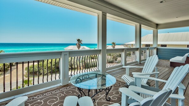 Un espace extérieur abrité, doté d’une table en verre et de chaises blanches, qui offre une vue sur la plage.