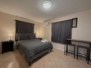 Un dormitorio con cama, mesitas de noche, escritorio y silla.