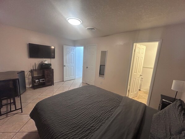 Un dormitorio con cama, televisión, escritorio y puerta que da a otra habitación.