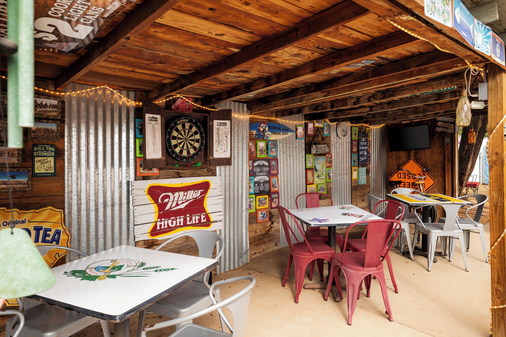 Un coin bar rustique avec des poutres en bois, un jeu de fléchettes et une enseigne publicitaire pour la bière Miller High Life.
