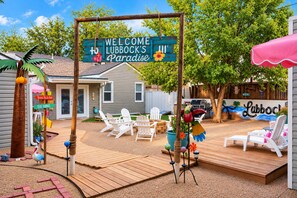 A backyard with a wooden deck, outdoor seating, and a welcome sign. - The Bung – A Little Slice of Paradise! 🦩🌺 (Lubbock)