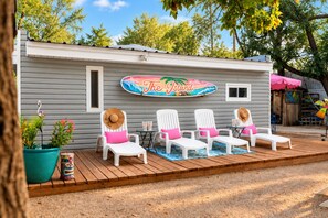 A small cabin with a surfboard sign reading 'The Island' and outdoor seating with chairs and cushions.