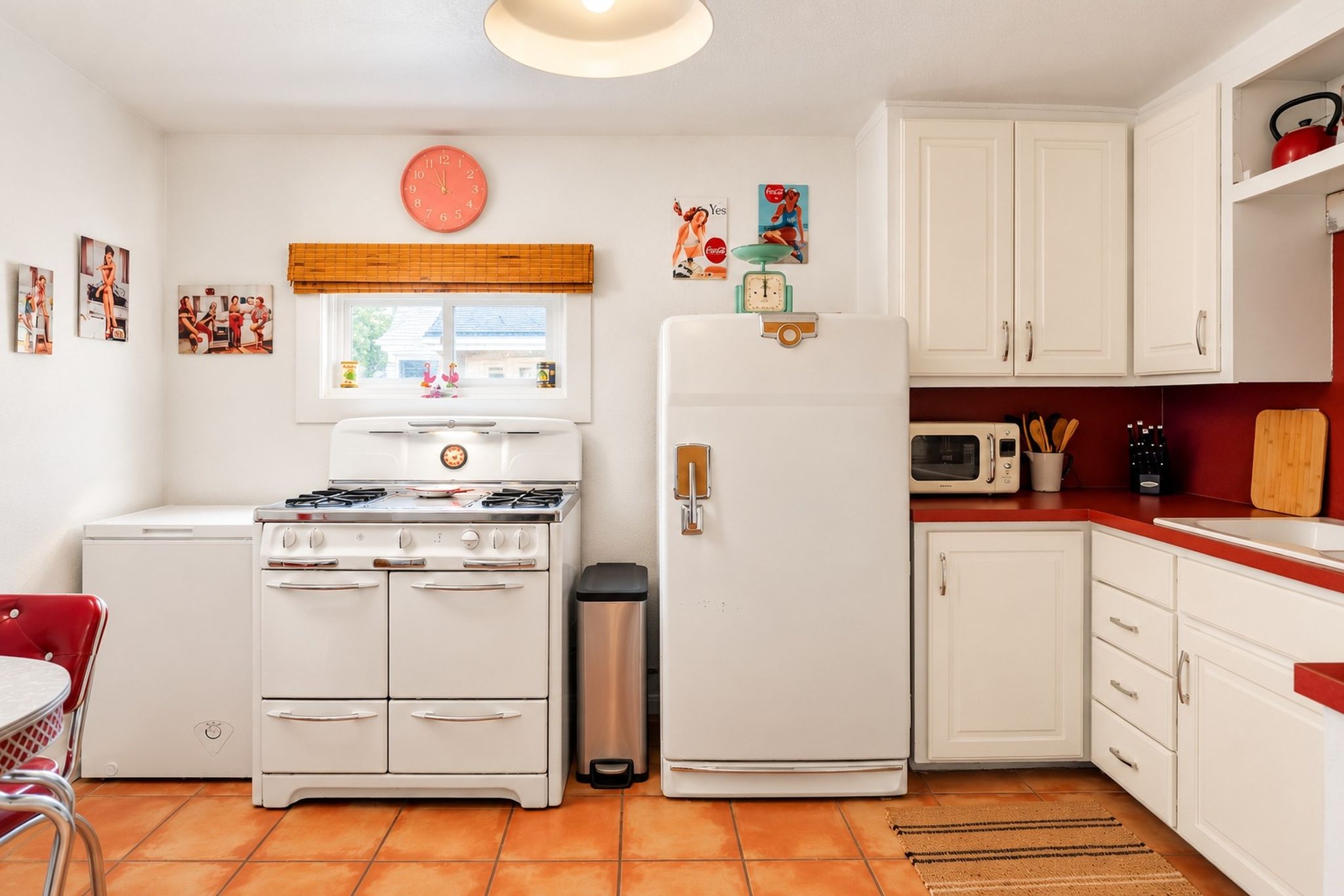 A kitchen with white cabinets, a stove, a refrigerator, a microwave, and a trash bin.