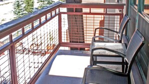 Ein Holzbalkon mit Metallgeländern, einer Sitzbank und Blick auf Bäume sowie ein Gebäude im Hintergrund.