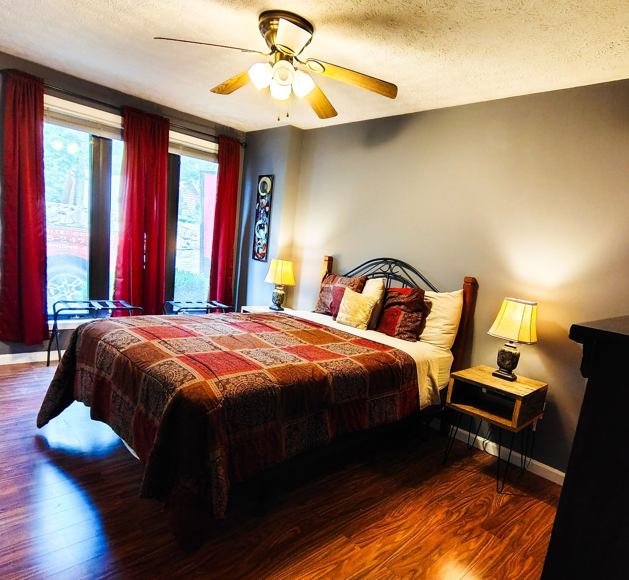 Une chambre à coucher avec un lit, deux lampes de chevet, un ventilateur de plafond et une fenêtre avec des rideaux.
