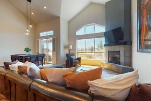 A spacious living room with a fireplace, a dining area, and a large window providing a view of the outdoors.