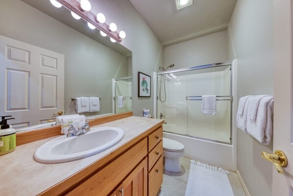 A bathroom with a large mirror, a sink, a toilet, and a shower.