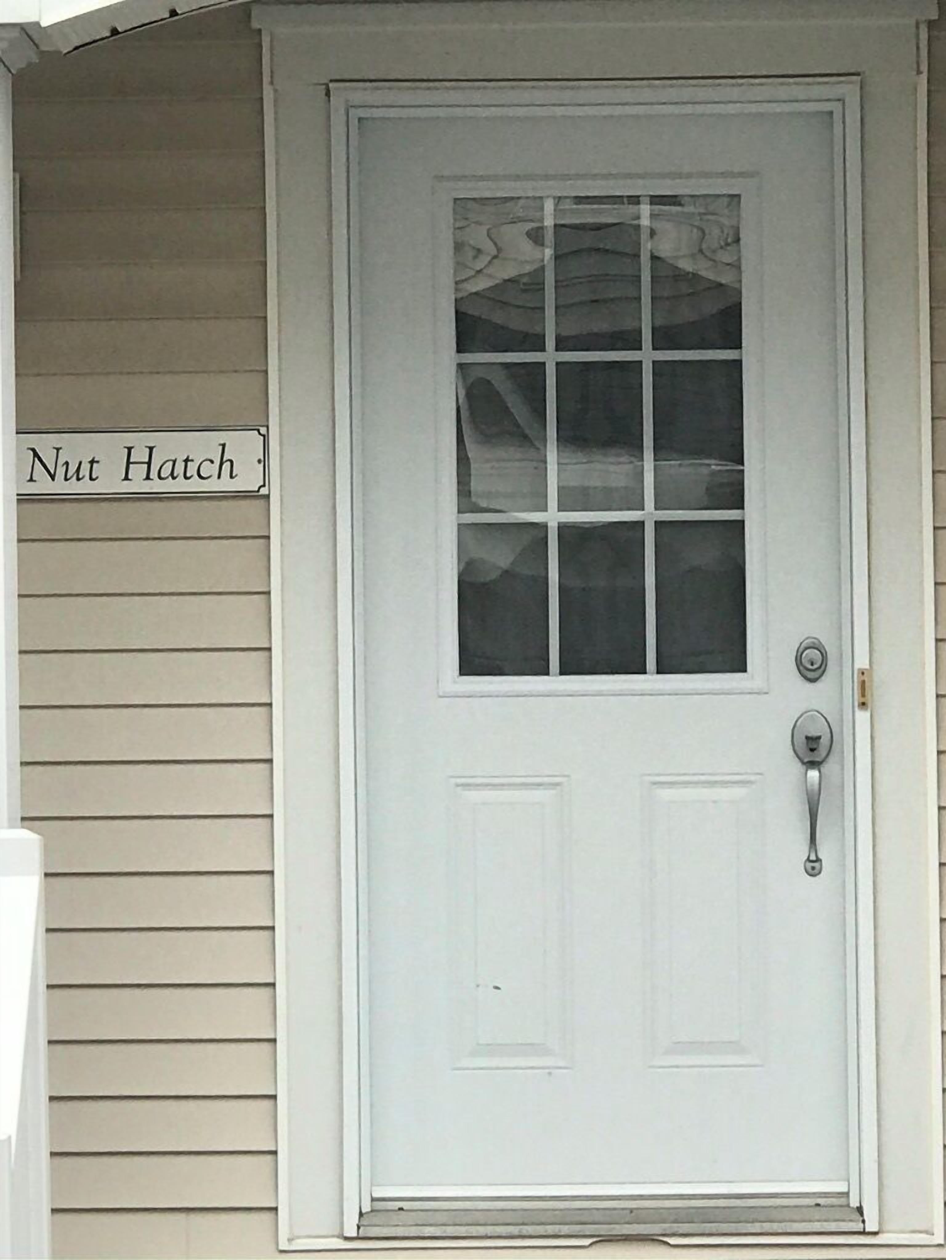 Une porte d’entrée blanche avec un panneau de verre et une poignée en métal. Une enseigne au-dessus de la porte indique « Nut Hatch ».