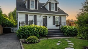 A two-story house with a dark roof, white siding, and black shutters. It has a front porch with steps and a mailbox. - Secret Garden Cottage in Old Town Niagara-on-the-Lake (Niagara-on-the-Lake)