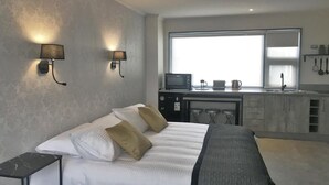 Ein modernes Hotelzimmer mit einem Bett, Nachttischen, einer Küchenzeile inklusive Mikrowelle und einem großen Fenster.