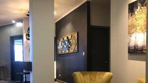 Eine moderne Lobby mit dunkler Wand, einem goldfarbenen Sessel, einem runden Couchtisch und einem Gemälde.
