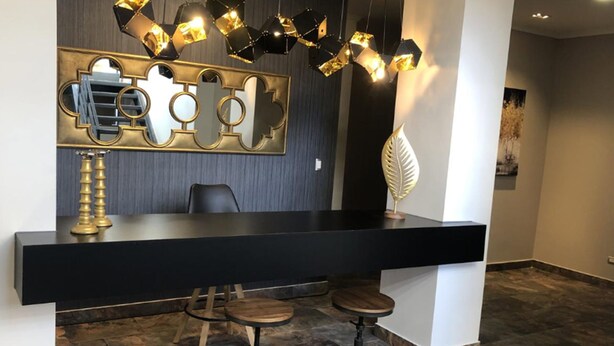 Eine moderne Bar mit schwarzem Tresen, zwei Barhocker und einem dekorativen Spiegel mit geometrischen Mustern.