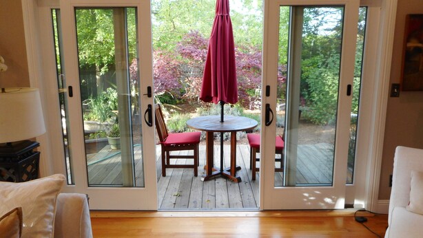 A room with a sliding glass door leading to a patio with a table and chairs, a red umbrella, and a garden view. - Harmony House - a serene place to relax and renew (Sebastopol)