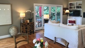 A living room with a sofa, a dining table with chairs, a TV, and a bookshelf. There is a sliding glass door leading to an outdoor area with a table and chairs. - Harmony House - a serene place to relax and renew (Sebastopol)