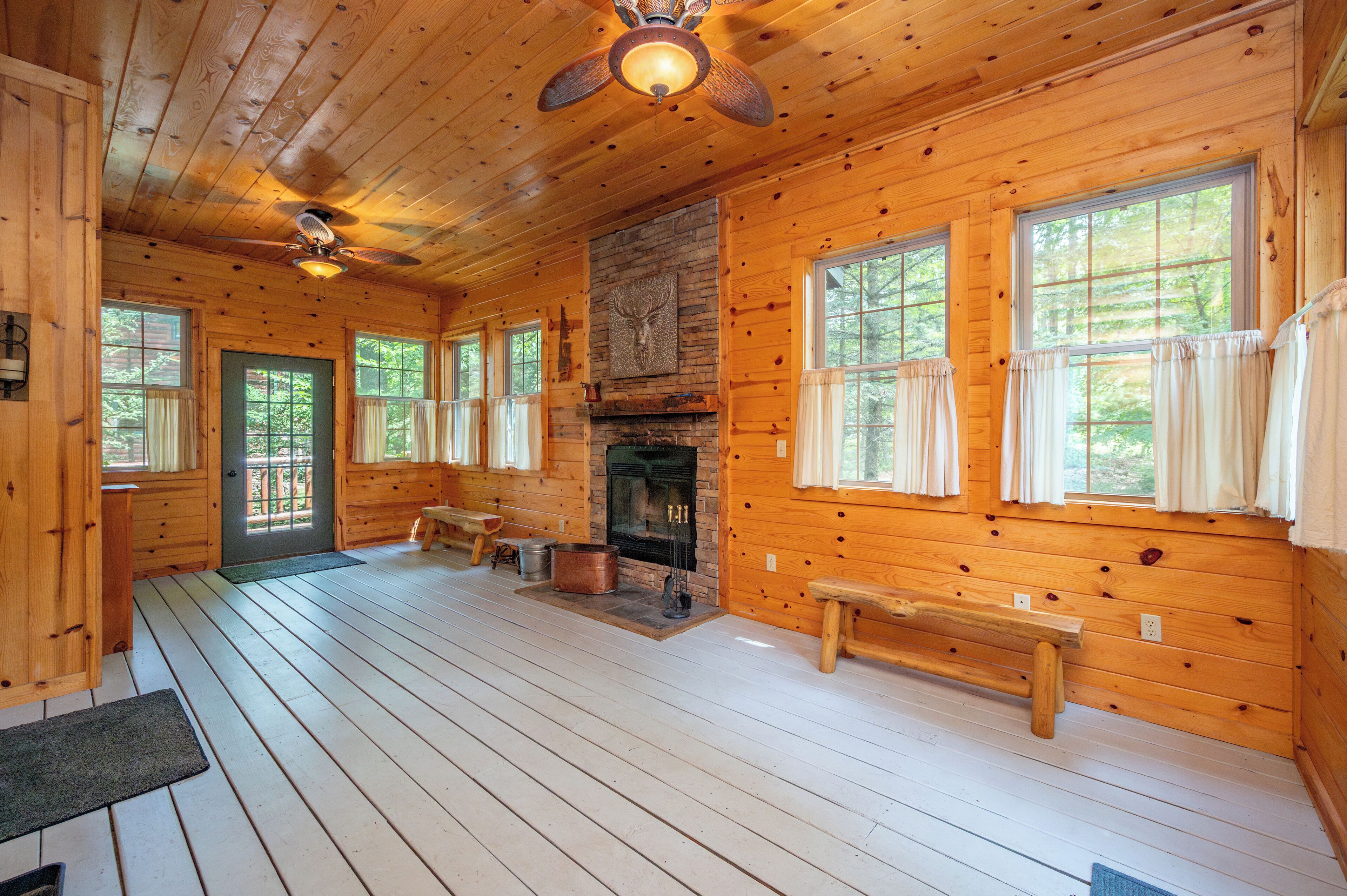 A log cabin interior with a fireplace, wooden floors, and large windows.