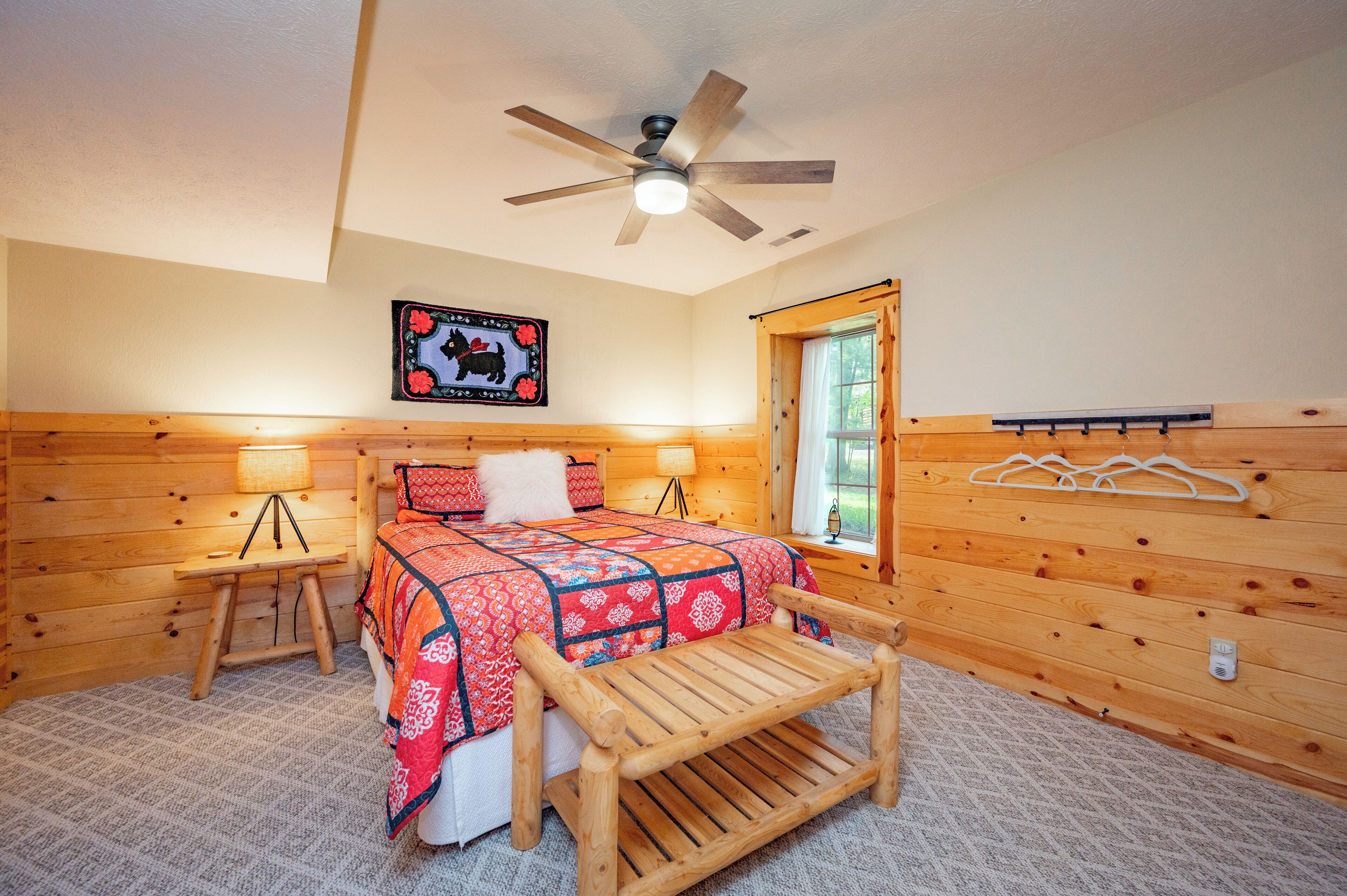 A cozy bedroom with a wooden bed, a ceiling fan, a window with a view, and a wall-mounted coat rack.