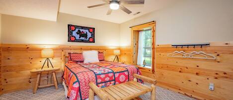 A cozy bedroom with a wooden bed, a ceiling fan, a window with a view, and a wall-mounted coat rack.