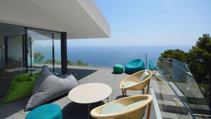 Een modern buitenzitgedeelte met een glazen balustrade, rieten meubilair en uitzicht op zee.