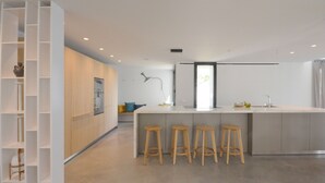 Een moderne keuken met een centraal eiland, houten krukken en een ingebouwde boekenkast.