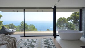 Een moderne badkamer met een groot bad, uitzicht op zee en een vloerkleed met een geometrisch patroon.