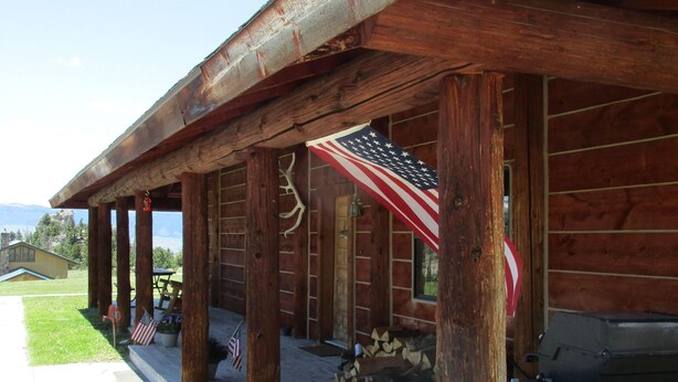 Une cabane en bois rustique, dotée d’un porche, d’un drapeau américain et d’un barbecue.