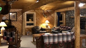 L’intérieur d’une cabane en rondins, avec une cheminée, des murs en bois, un coin salon confortable et des décorations en forme de bois de cerf.