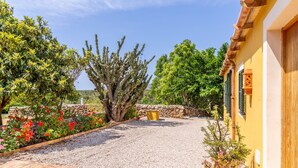 A courtyard with a gravel path, a stone wall, and a yellow building with green shutters. - Ses Cases Son Blat, 5StarsHome Mallorca Estate (Manacor)