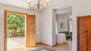 A spacious hallway with a wooden door leading to a garden, a chandelier, a green sofa, and a small round table. - Ses Cases Son Blat, 5StarsHome Mallorca Estate (Manacor)