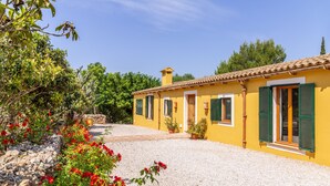 A yellow building with green shutters, a gravel driveway, and red flowers in the foreground. - Ses Cases Son Blat, 5StarsHome Mallorca Estate (Manacor)