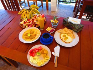 Una mesa de desayuno con platos de comida, un frutero, un vaso de jugo y una taza de café.