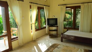 Una habitación con una cama, un televisor sobre un mueble bajo y una ventana con cortinas.