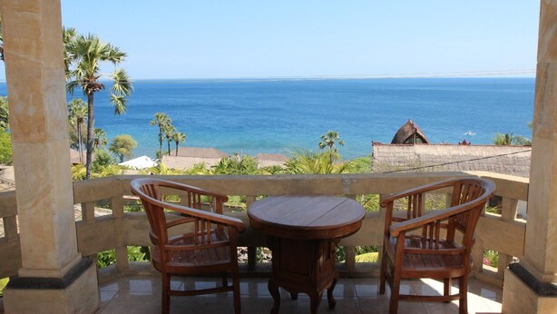 Un balcón con mesa y sillas de madera que da a vistas de la costa.