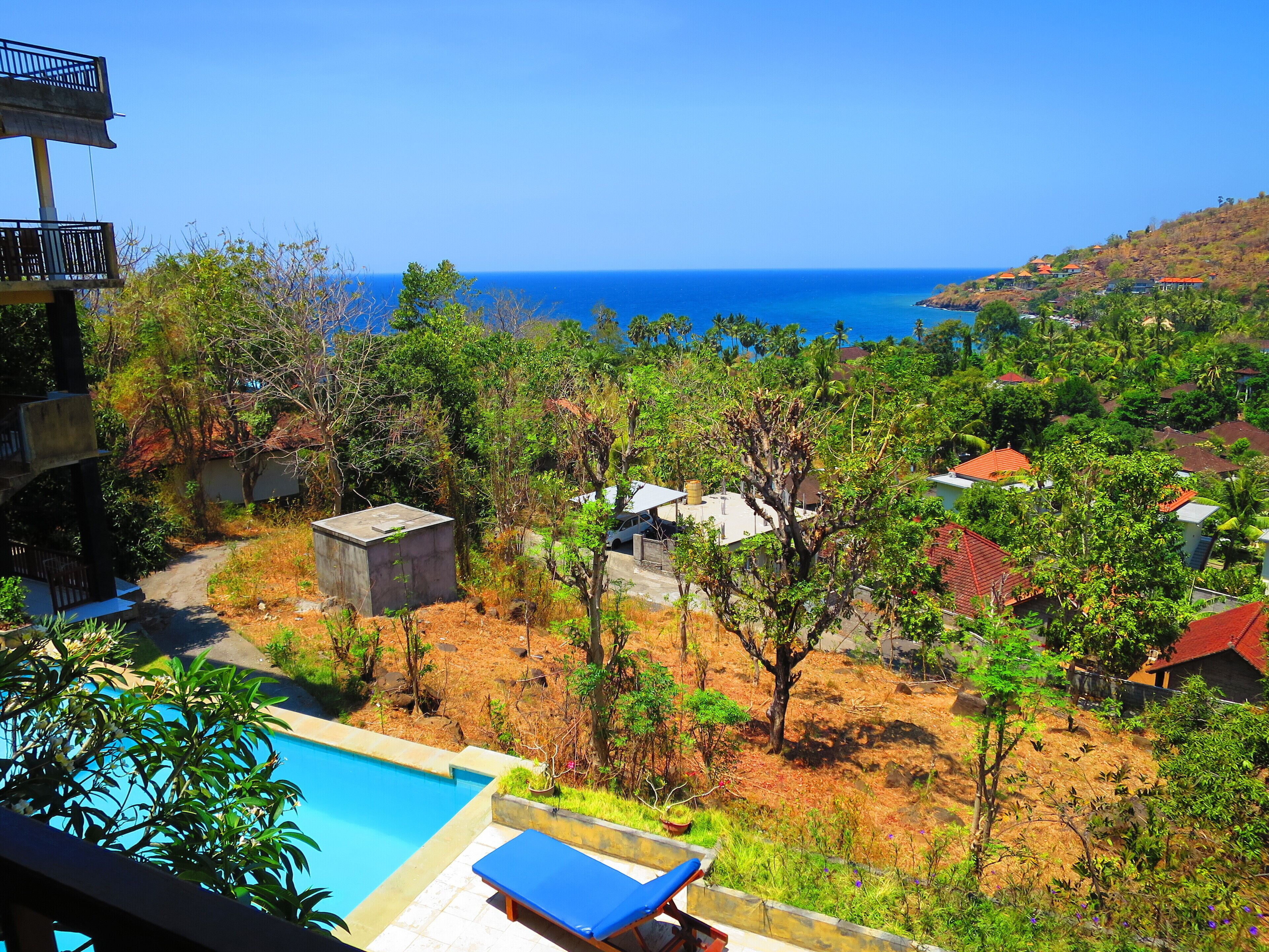 A resort with a swimming pool, a view of the ocean, and a hillside with buildings.