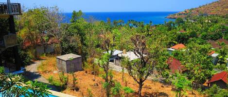 A resort with a swimming pool, a view of the ocean, and a hillside with buildings.