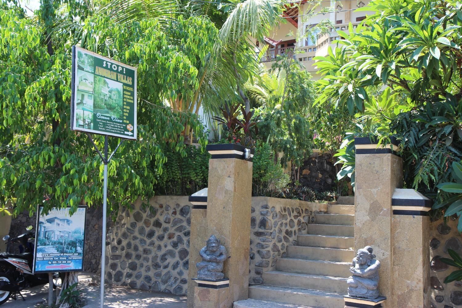 A stone staircase leading to a building entrance, flanked by statues and surrounded by lush greenery.