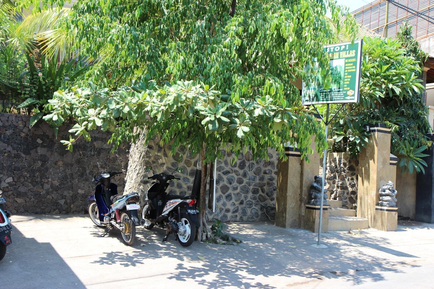 A stone wall with a signboard, parked motorcycles, and a statue.