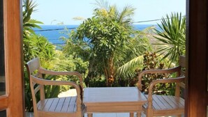 Una mesa de madera y dos sillas en un patio con baldosas, con vistas al océano y palmeras.