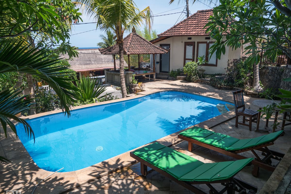 A swimming pool with lounge chairs, a covered seating area, and a view of the sea.