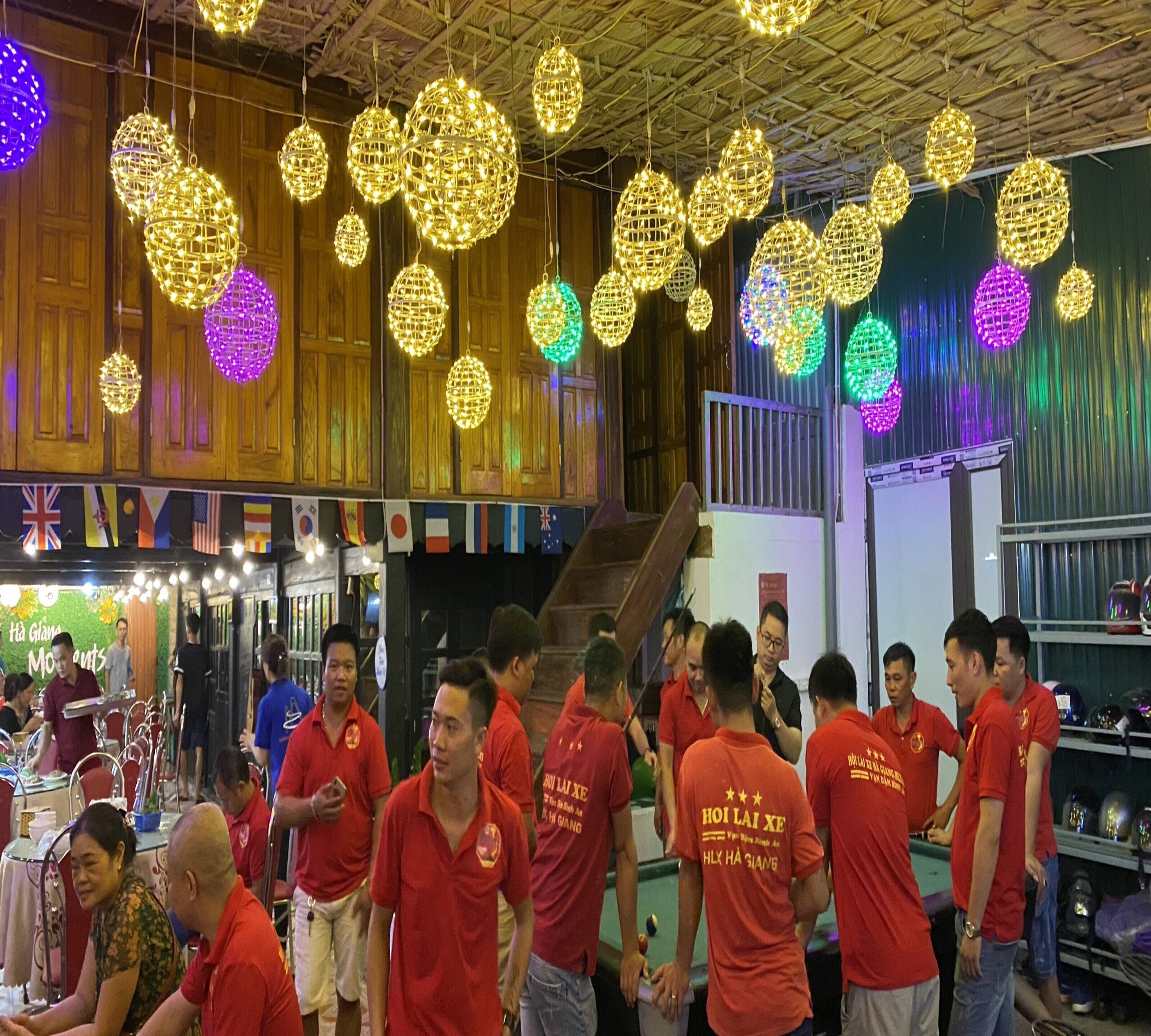 Un grupo de personas con camisetas rojas reunidas en una habitación con paneles de madera y lámparas esféricas colgantes.