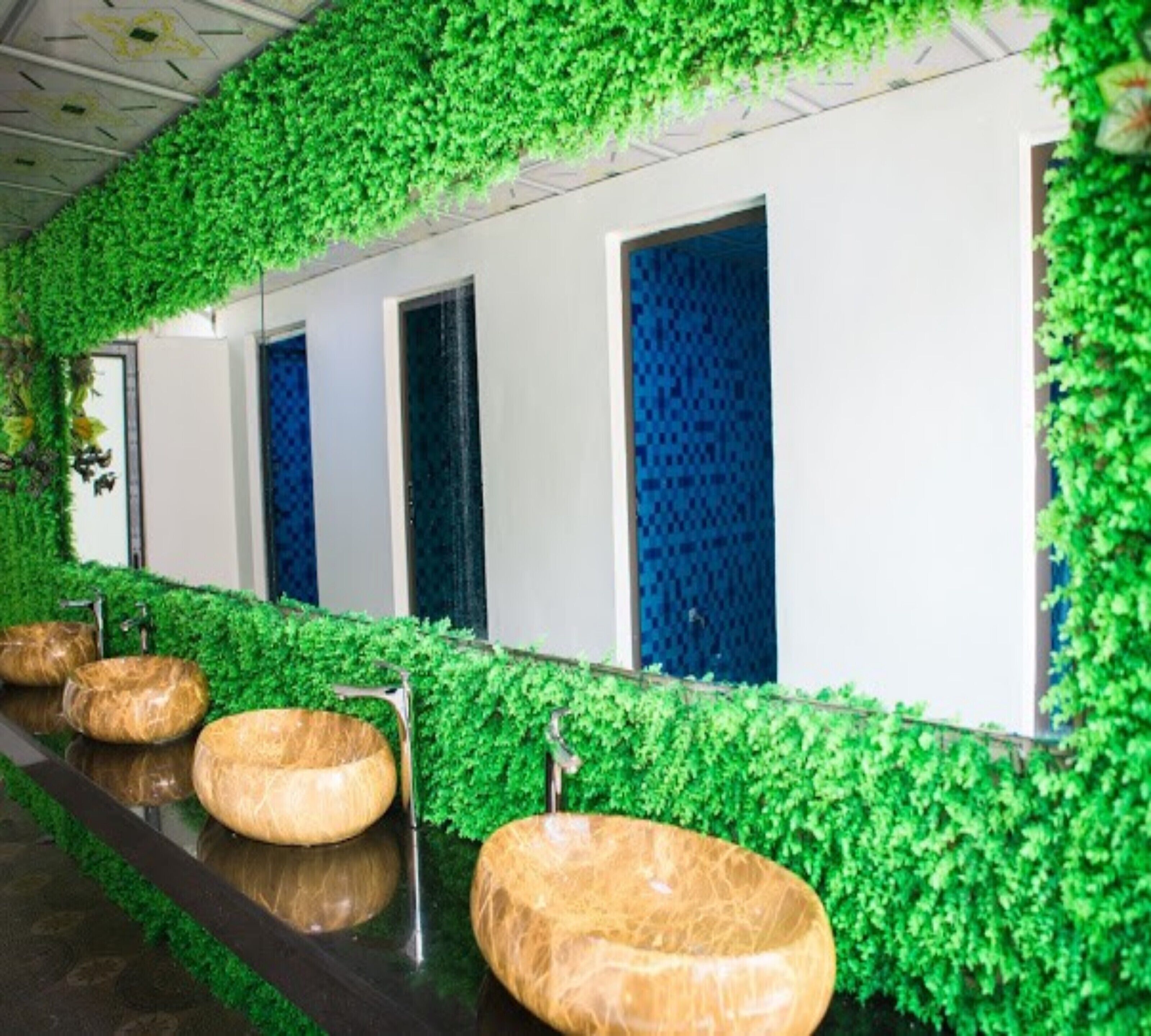 A bathroom with green foliage walls, multiple sinks, and blue patterned curtains.