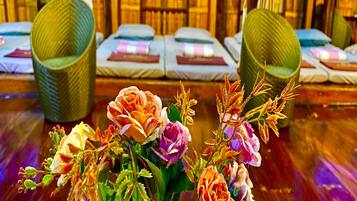 Hotelkamer met houten vloer, twee groene geweven stoelen, een bed met wit beddengoed en een bloemenboeket op de voorgrond.